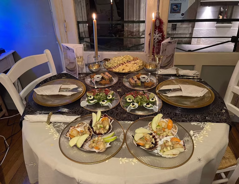 A candlelit dinner table set for four with gold-rimmed plates, seafood appetizers, deviled eggs as a festive starter, leafy greens, and wine glasses. Two lit candles, luxury decorations, and elegant dishes create a cozy yet artistic ambiance.