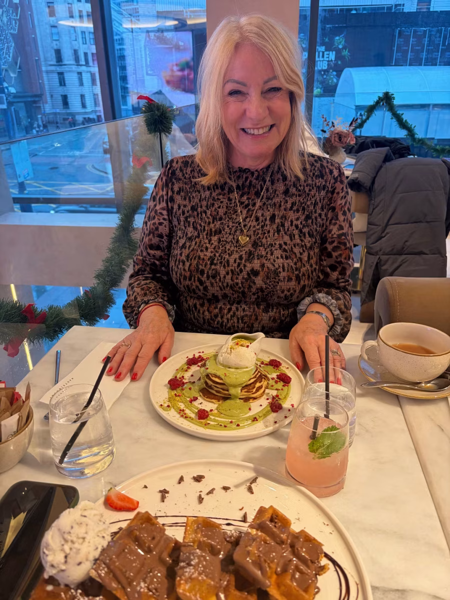 a smiling woman with blonde hair, wearing a leopard print top, sits at a table in a modern cafe decorated with christmas garland. in front of her are divine desserts—pancakes, waffles with whipped cream and chocolate sauce—perfect for an indulgent haute dolci restaurant review. A smiling woman with blonde hair, wearing a leopard-print top, sits at a table in a modern cafe decorated with Christmas garland. In front of her are divine desserts—pancakes, waffles with whipped cream and chocolate sauce—perfect for an indulgent HAUTE DOLCI restaurant review.
